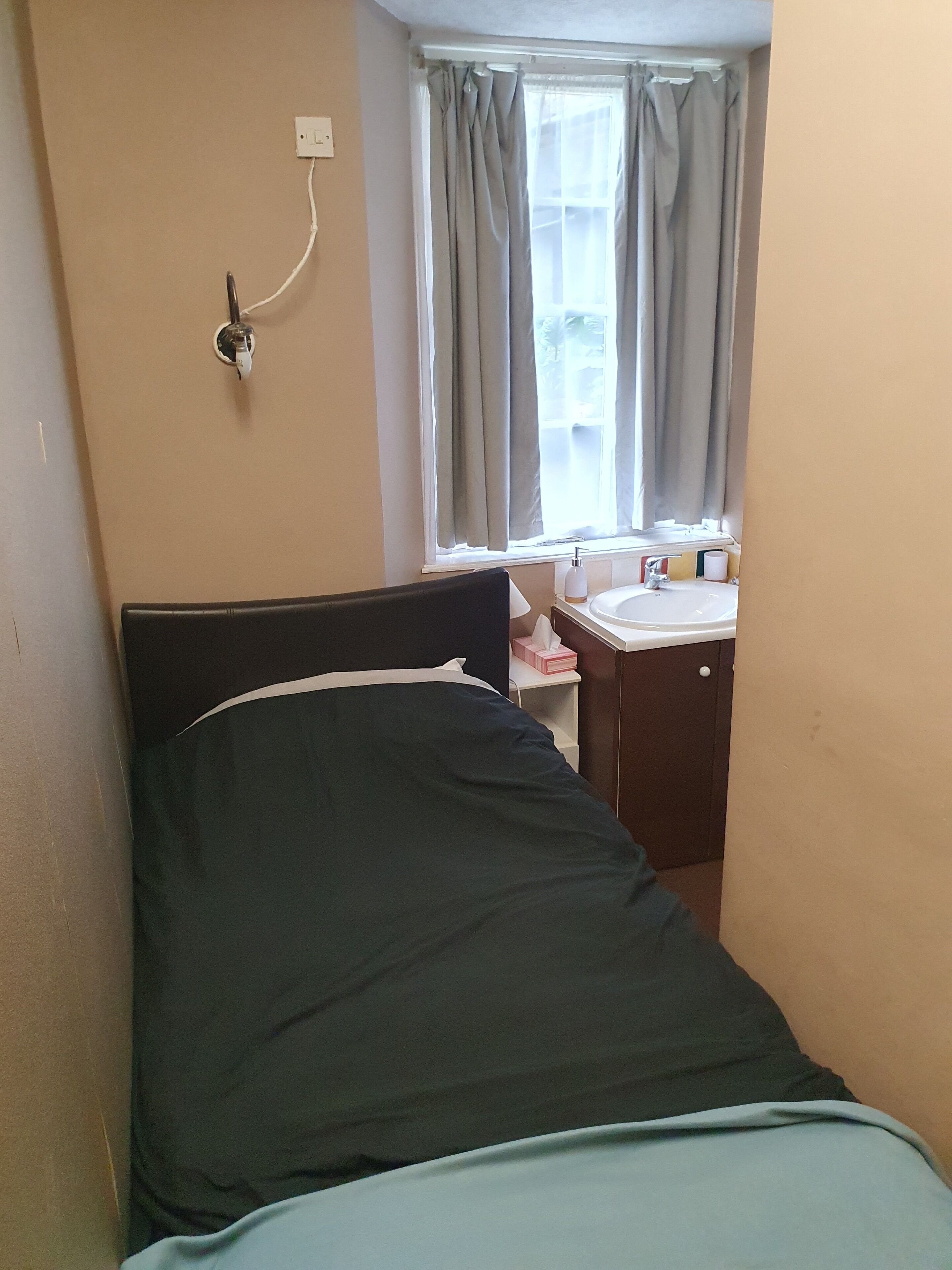 Une petite chambre avec un lit simple, une fenêtre, une table de chevet et un lavabo.