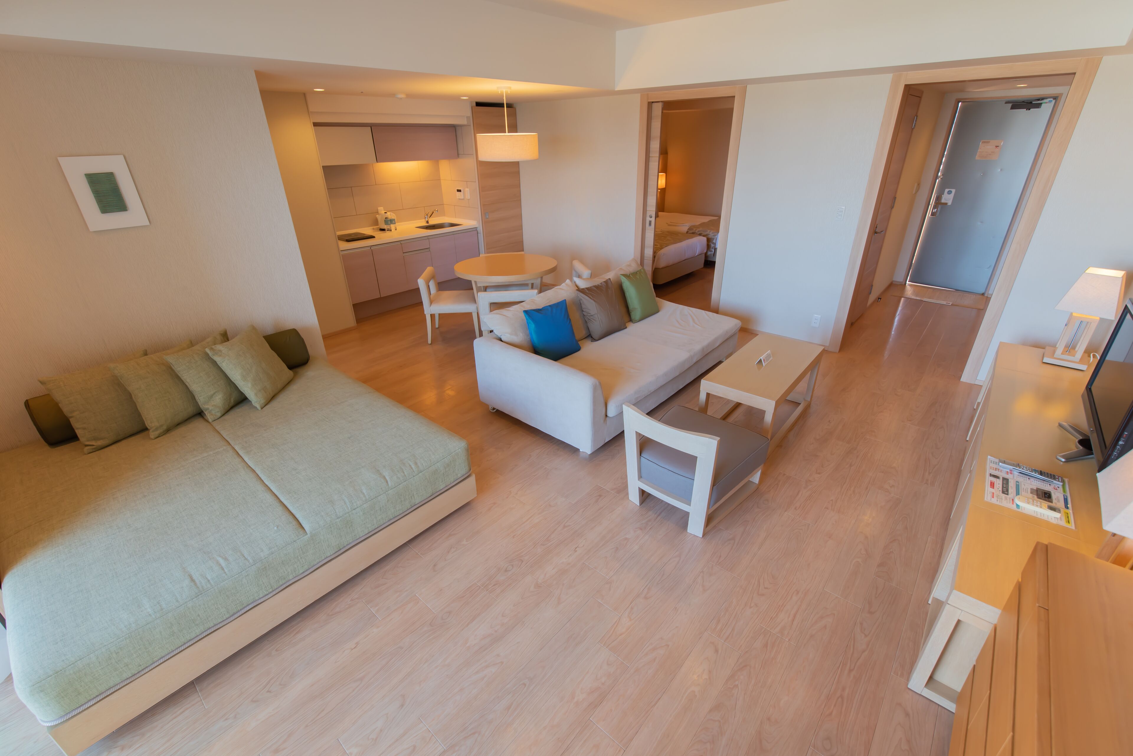 A modern apartment with a large bed, a sofa, a dining table, and a kitchen area.