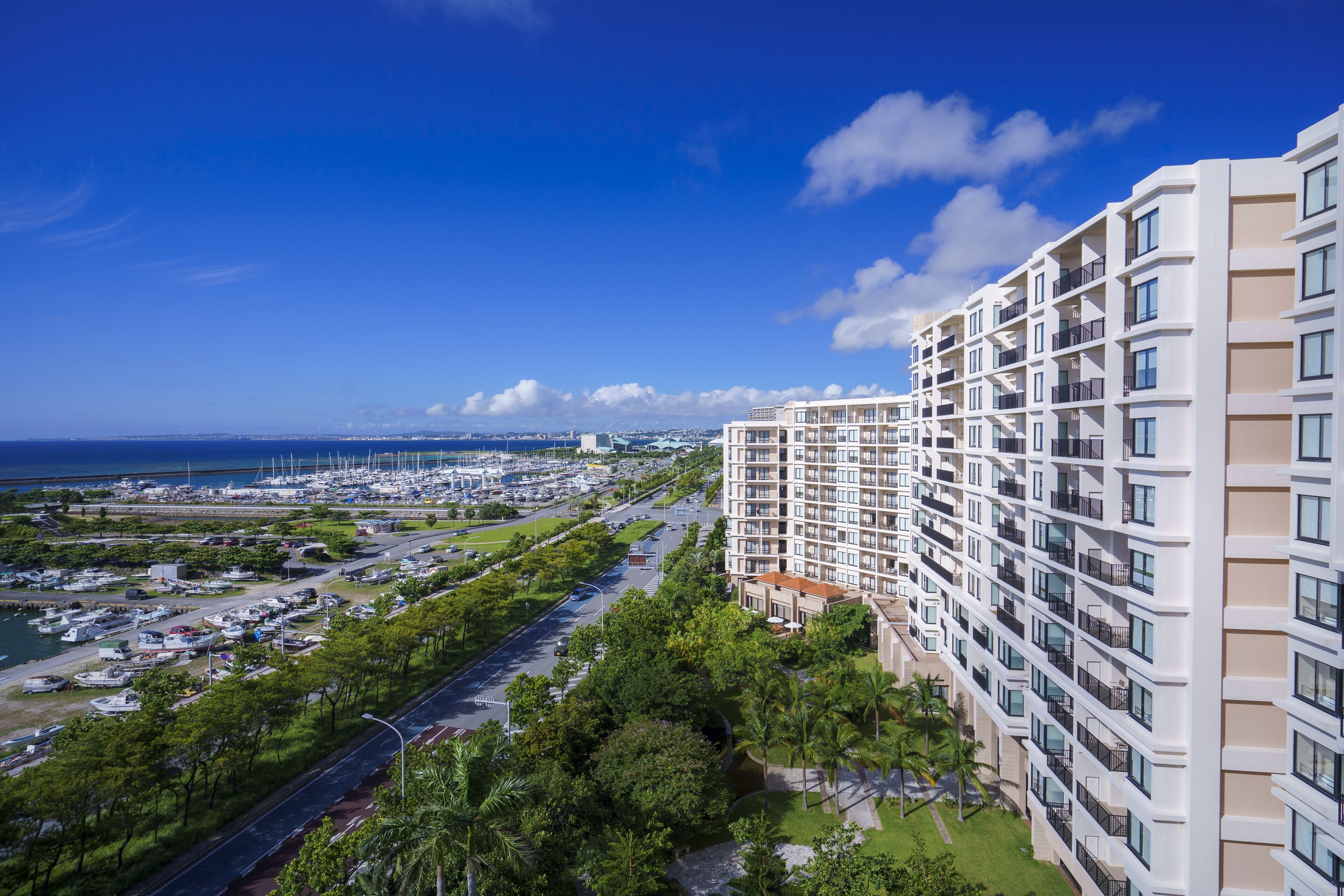 A high-rise hotel with multiple balconies, a marina with boats, and a clear blue sky.
