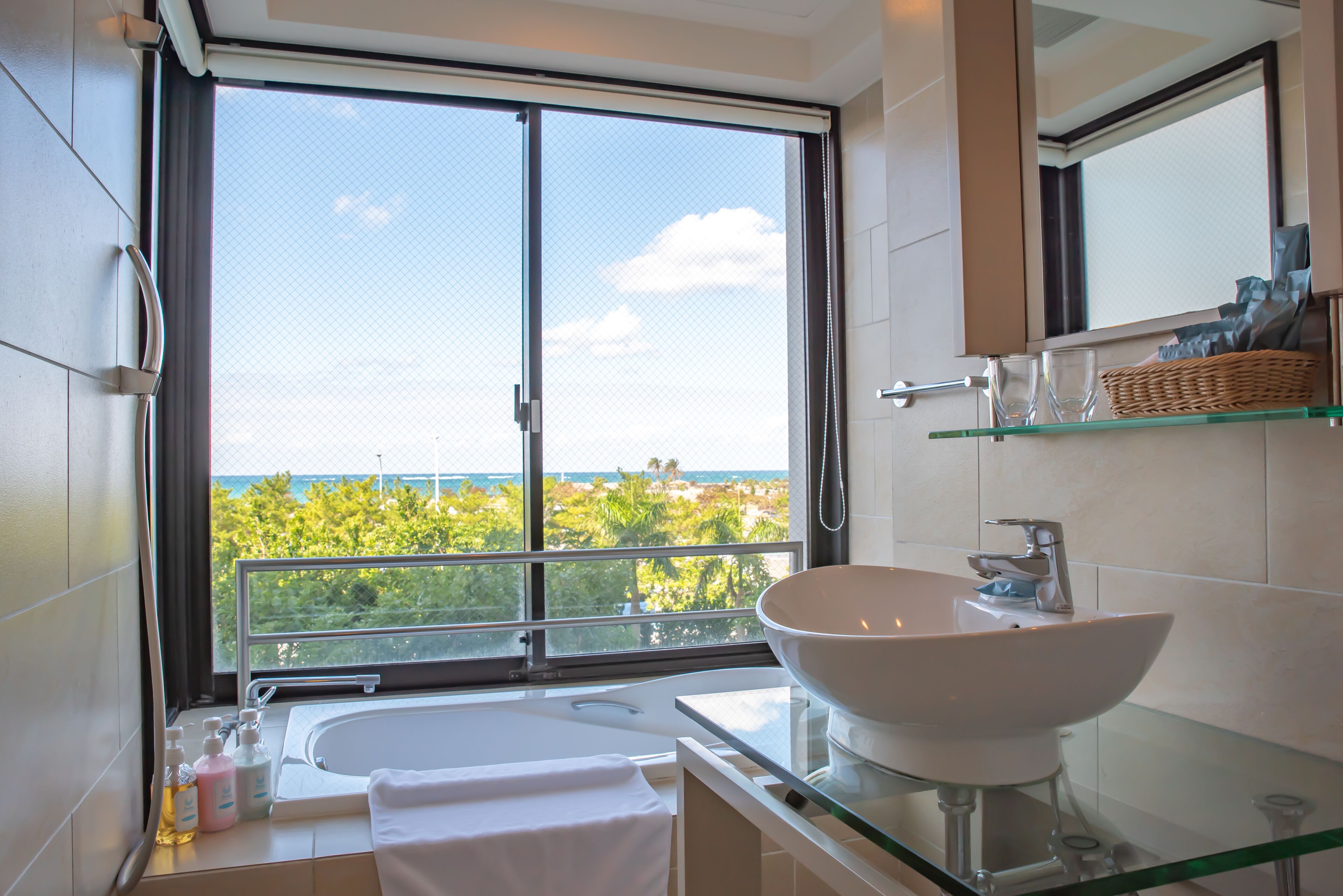 A modern bathroom with a large window, a white sink, and a glass shower enclosure.
