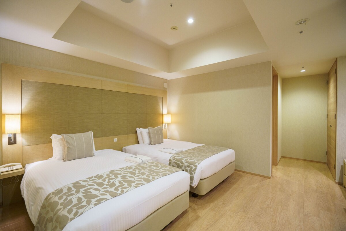 Una habitación de hotel con dos camas, cabeceros de madera, lámparas de noche y suelo de madera.