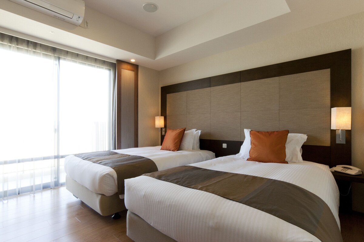 Habitación de hotel con dos camas, un ventanal grande y un diseño moderno.