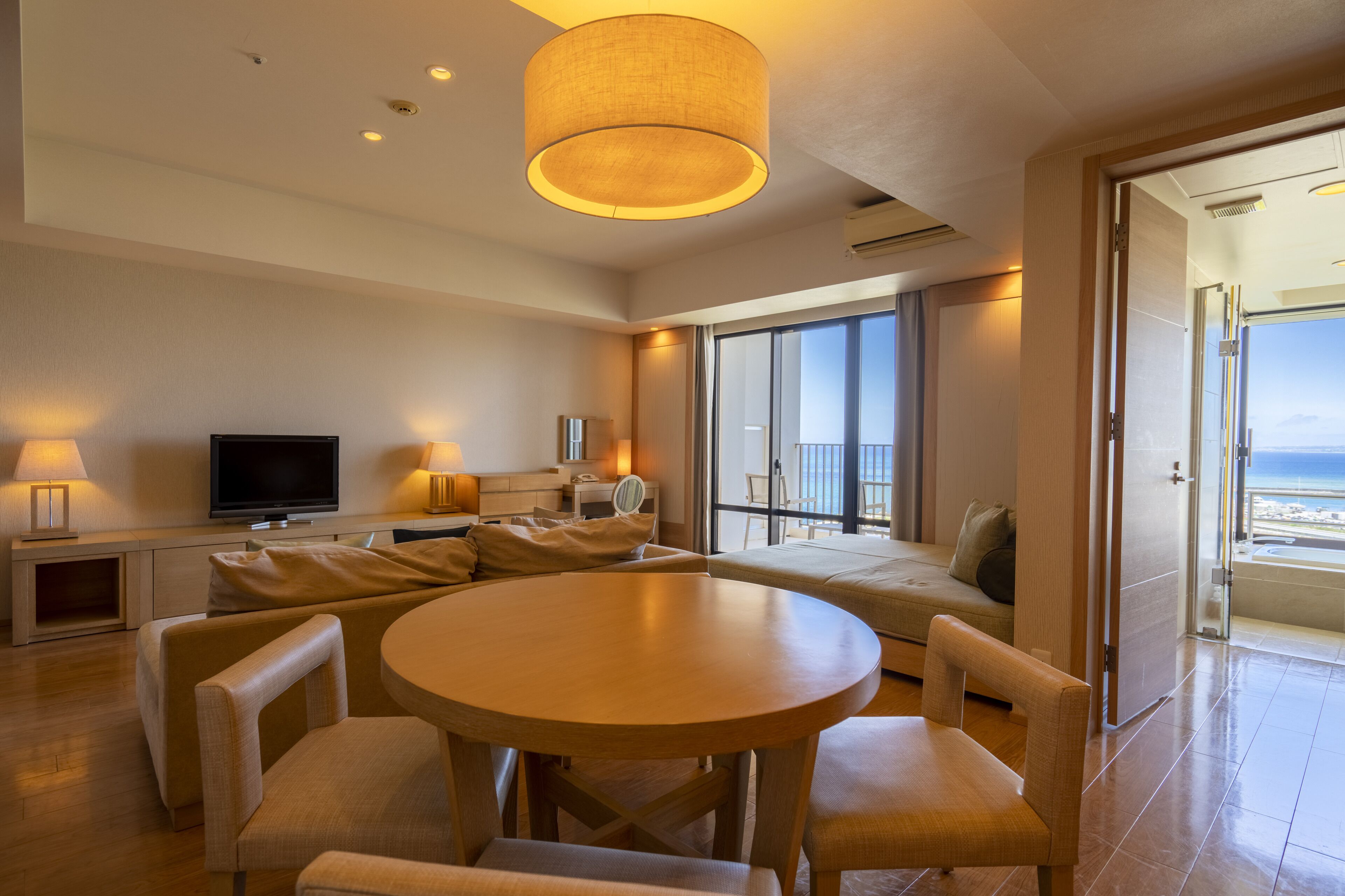 A modern hotel room with a large balcony, a round dining table, and a television.