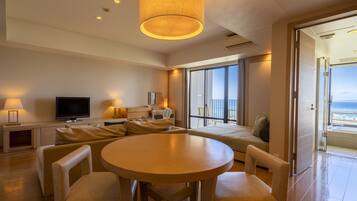 A modern hotel room with a large balcony, a round dining table, and a television.