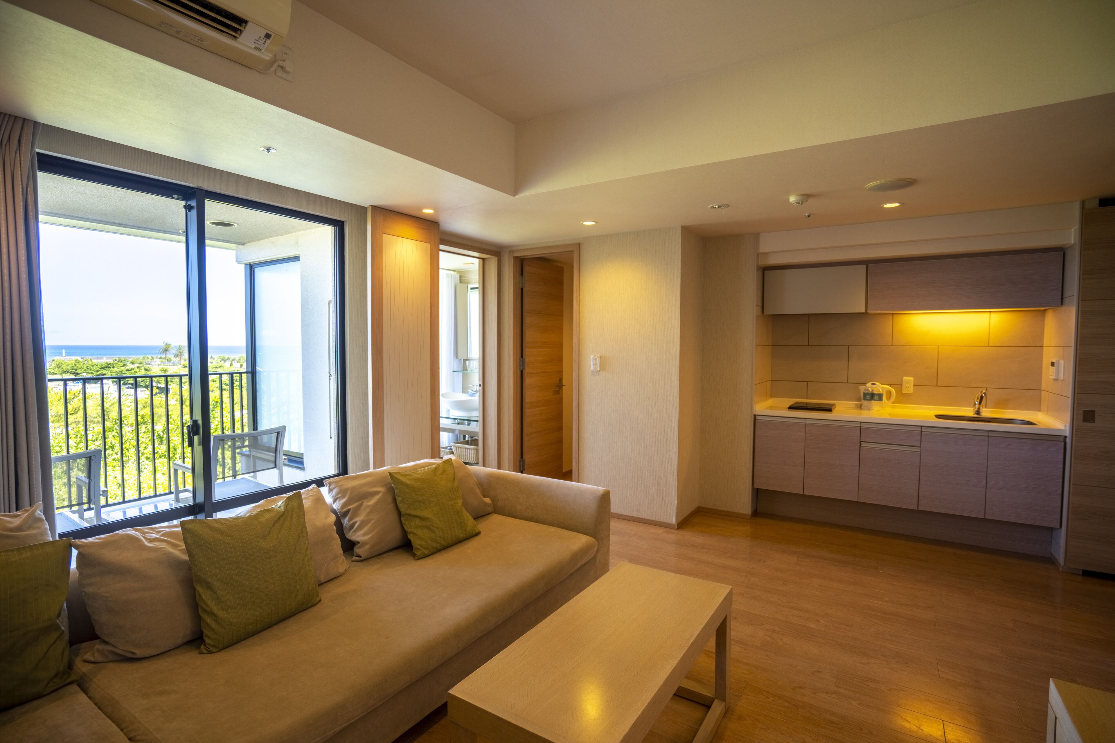 A modern living room with a sofa, a coffee table, and a kitchen area with cabinets and a sink.