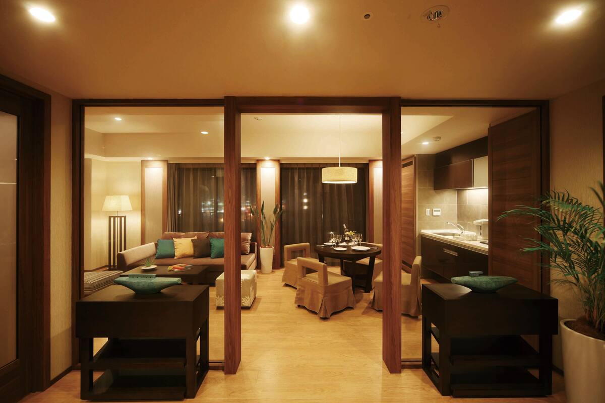 Una habitación de hotel moderna con zona de comedor, un conjunto de sofás y una cocina.
