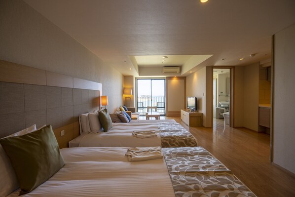 Habitación de hotel con una cama grande, una cama más pequeña, un sofá, un escritorio y un baño visible a través de una puerta abierta.