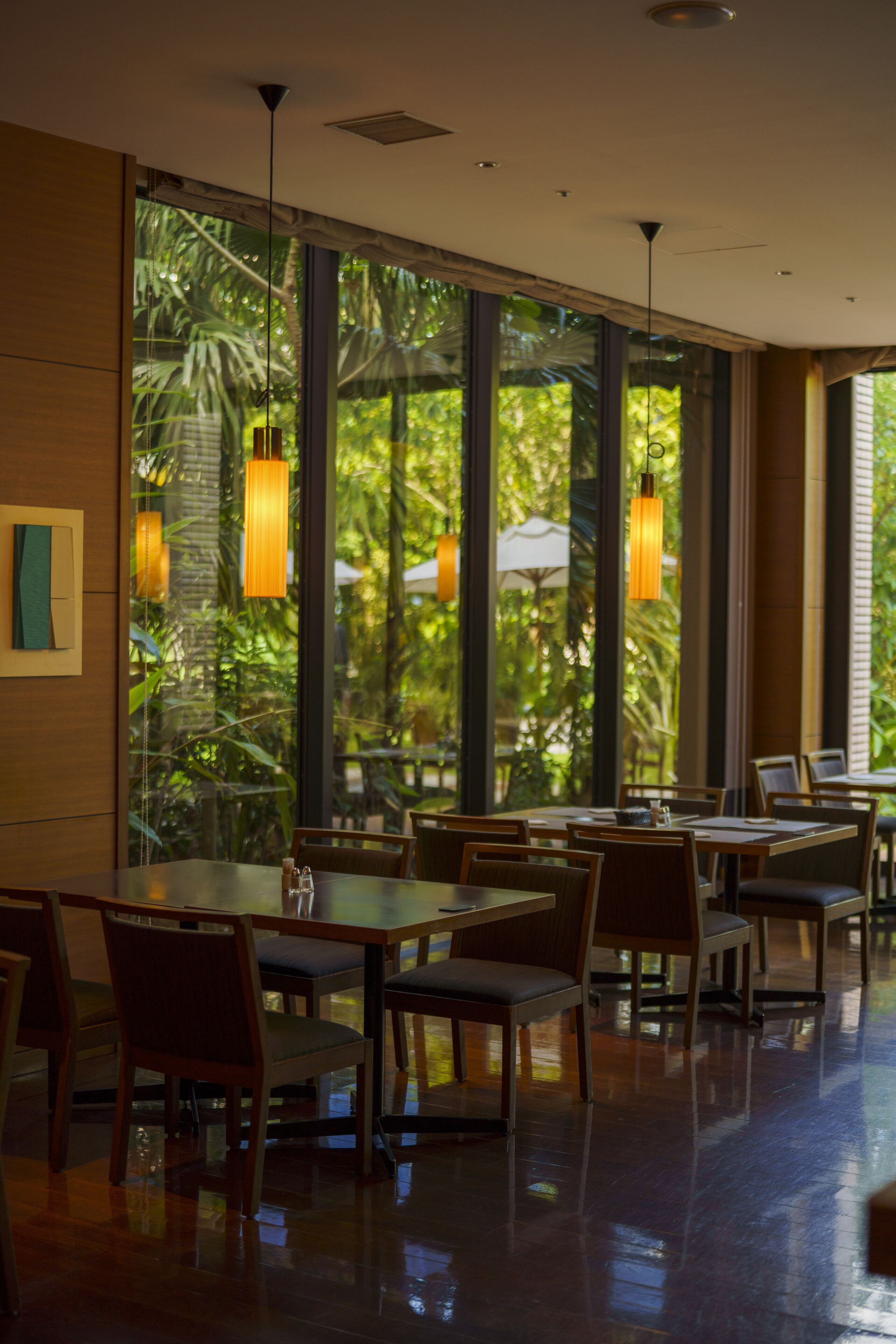 Un restaurante con amplios ventanales, mesas de madera y lámparas colgantes.