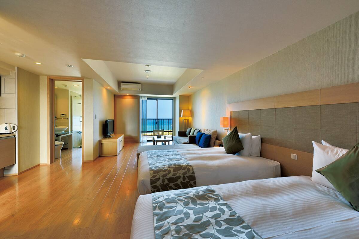 Habitación de hotel con dos camas, un escritorio y vista al mar.