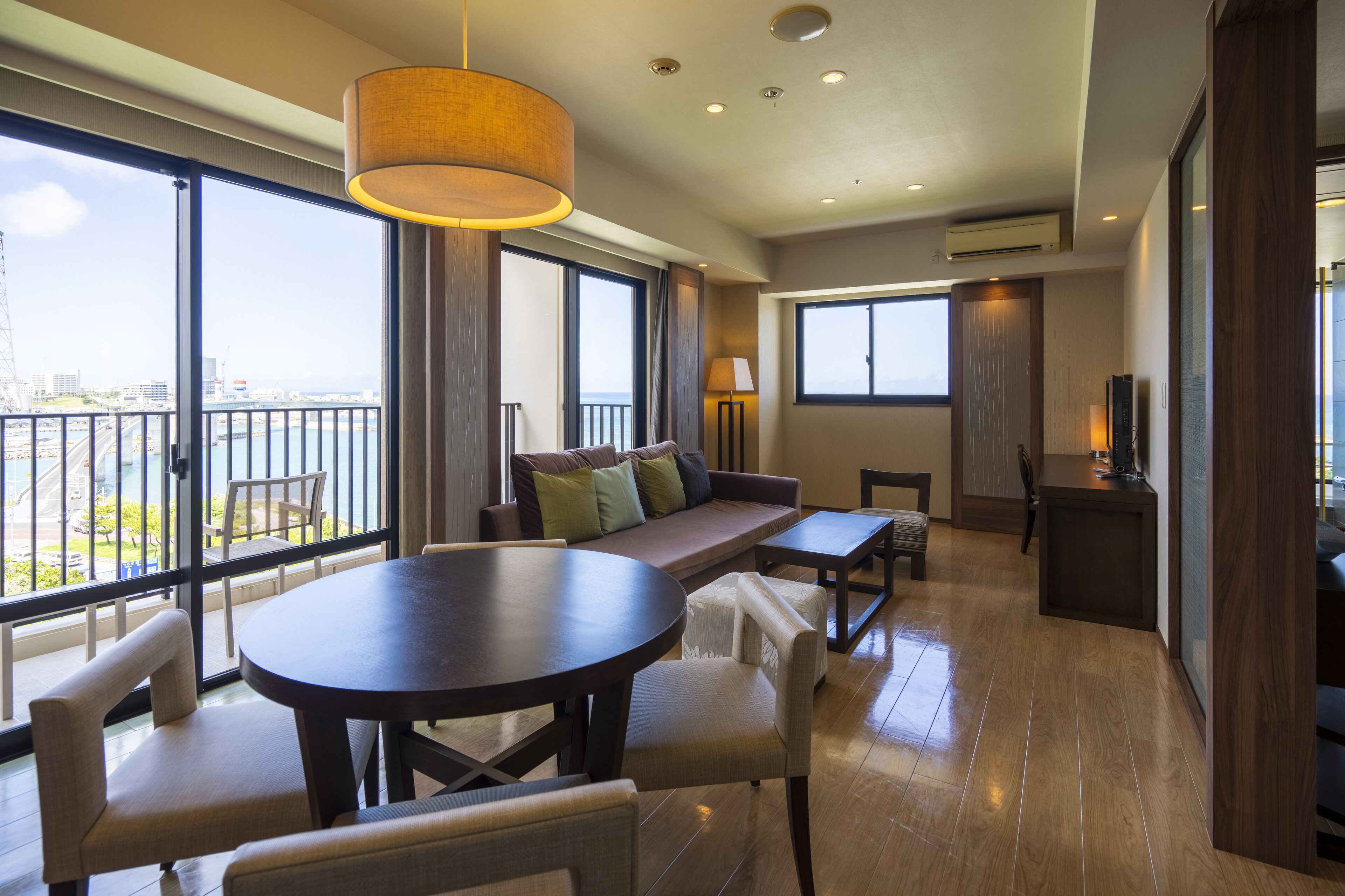 A spacious room with a balcony, a sofa, a dining table, and a TV.