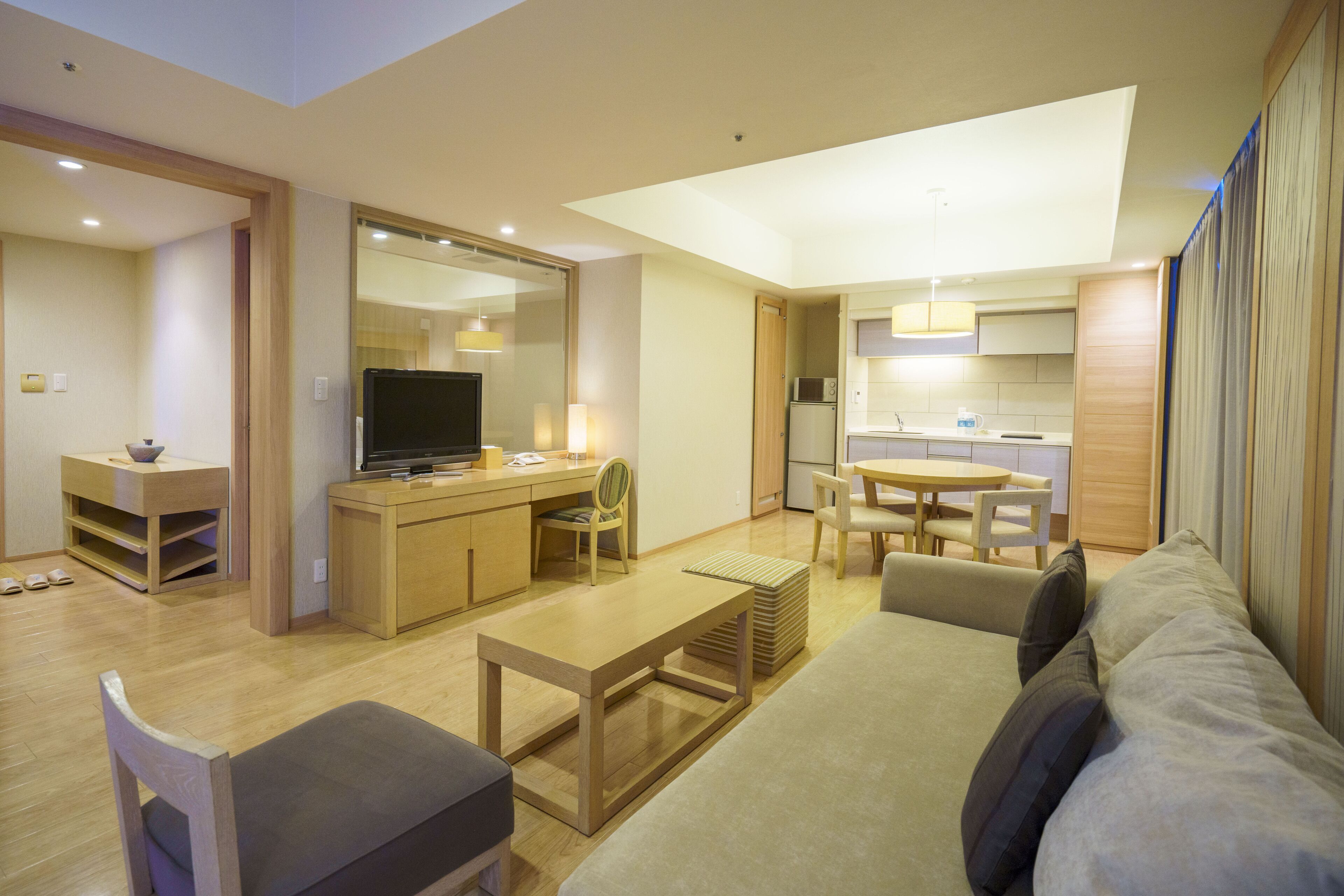 A modern living room with a sofa, a coffee table, a TV, and a dining area with chairs and a table.