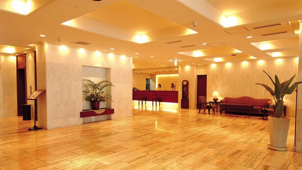 A spacious lobby with a wooden floor, a reception desk, a sofa, and a large potted plant. - Ryukyu Sun Royal Hotel (Naha)