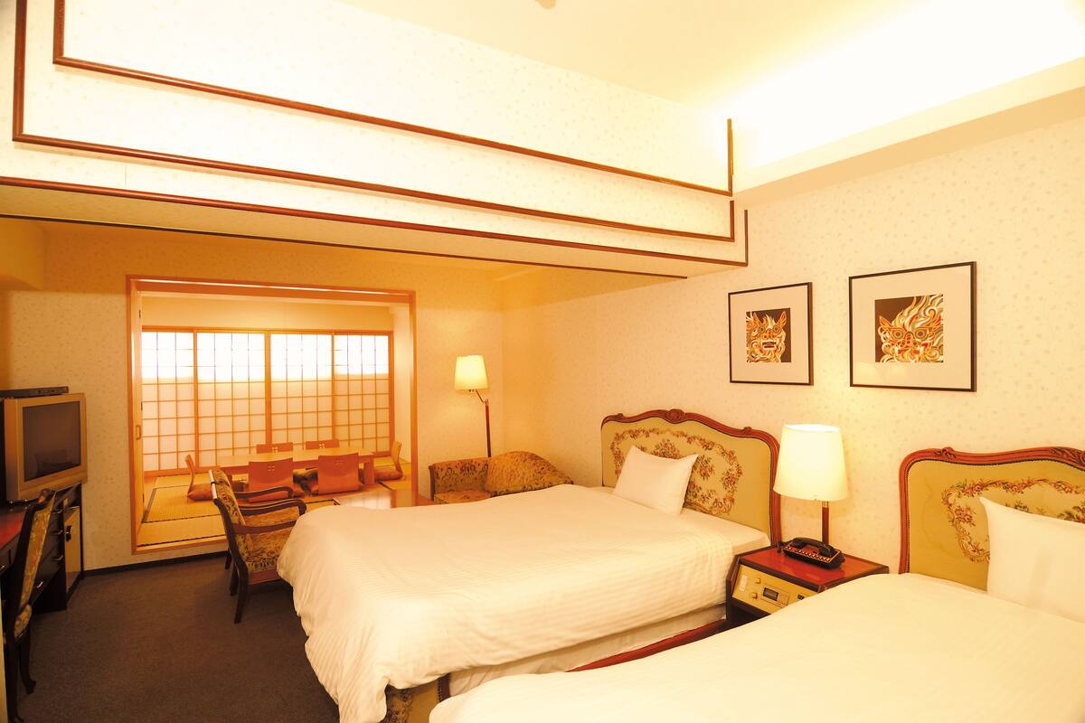 A hotel room with two beds, a desk, a chair, a television, and two framed pictures on the wall.