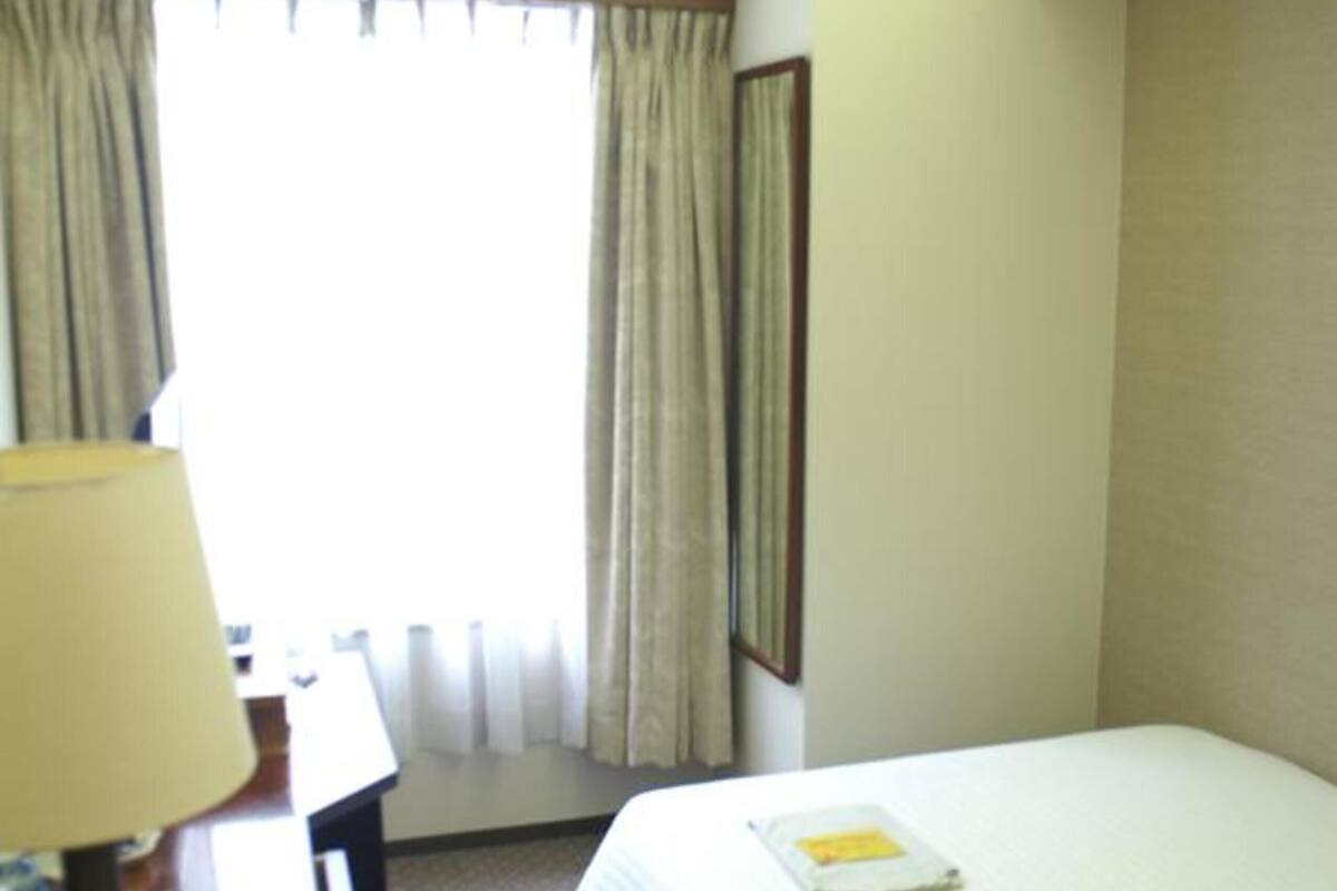 A hotel room with a bed, a desk with a lamp, and a window with curtains.