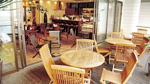 A restaurant with wooden tables and chairs, a bar area, and a view through a glass wall. - Ryukyu Sun Royal Hotel (Naha)