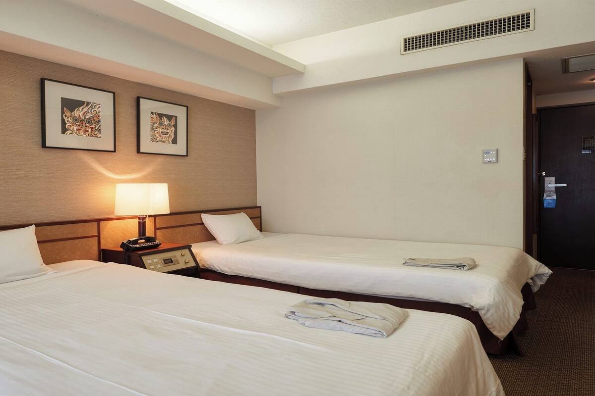 A hotel room with two beds, a nightstand with a lamp, and two framed pictures on the wall.