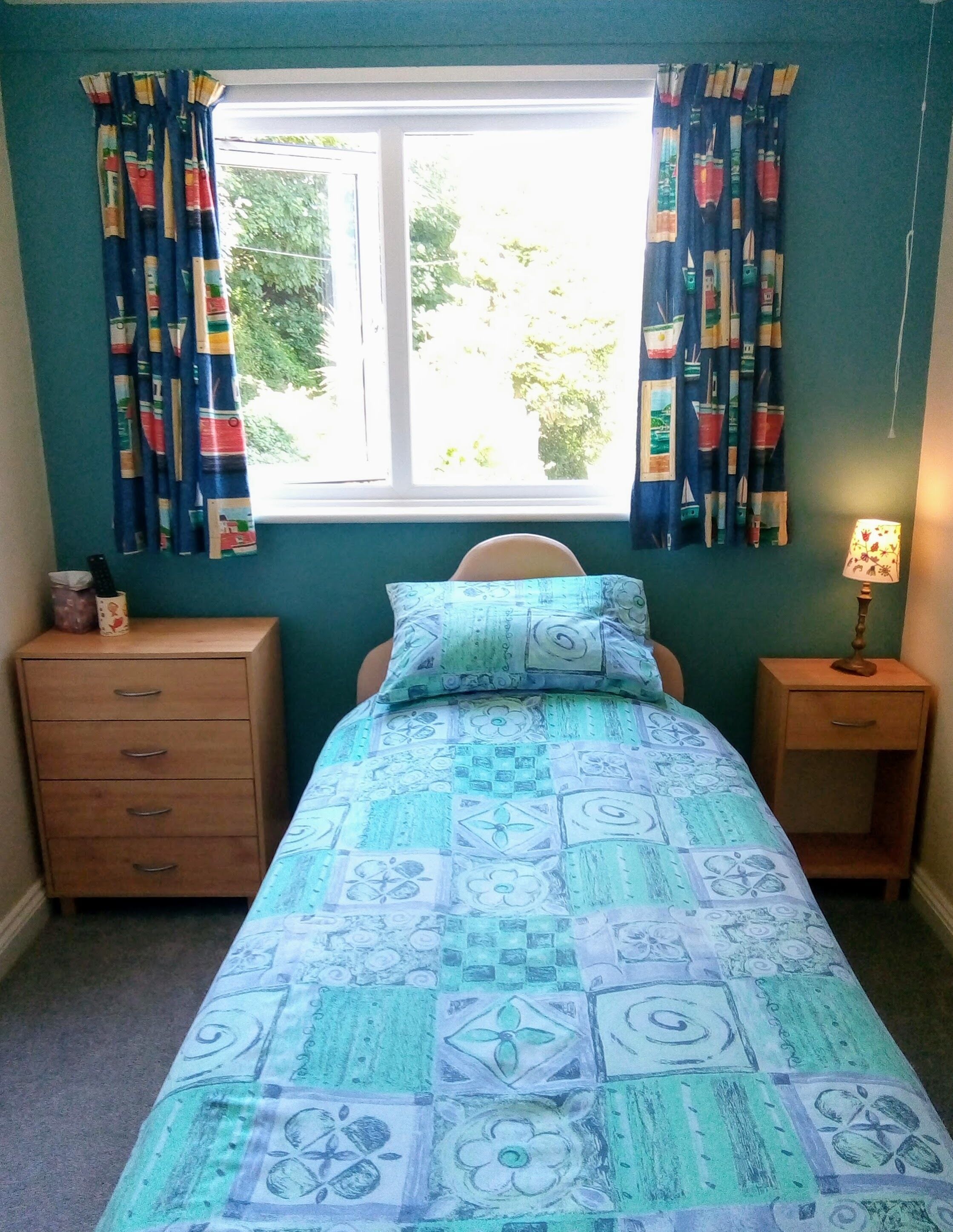 A bedroom with a bed, two nightstands, a dresser, and a window with curtains.