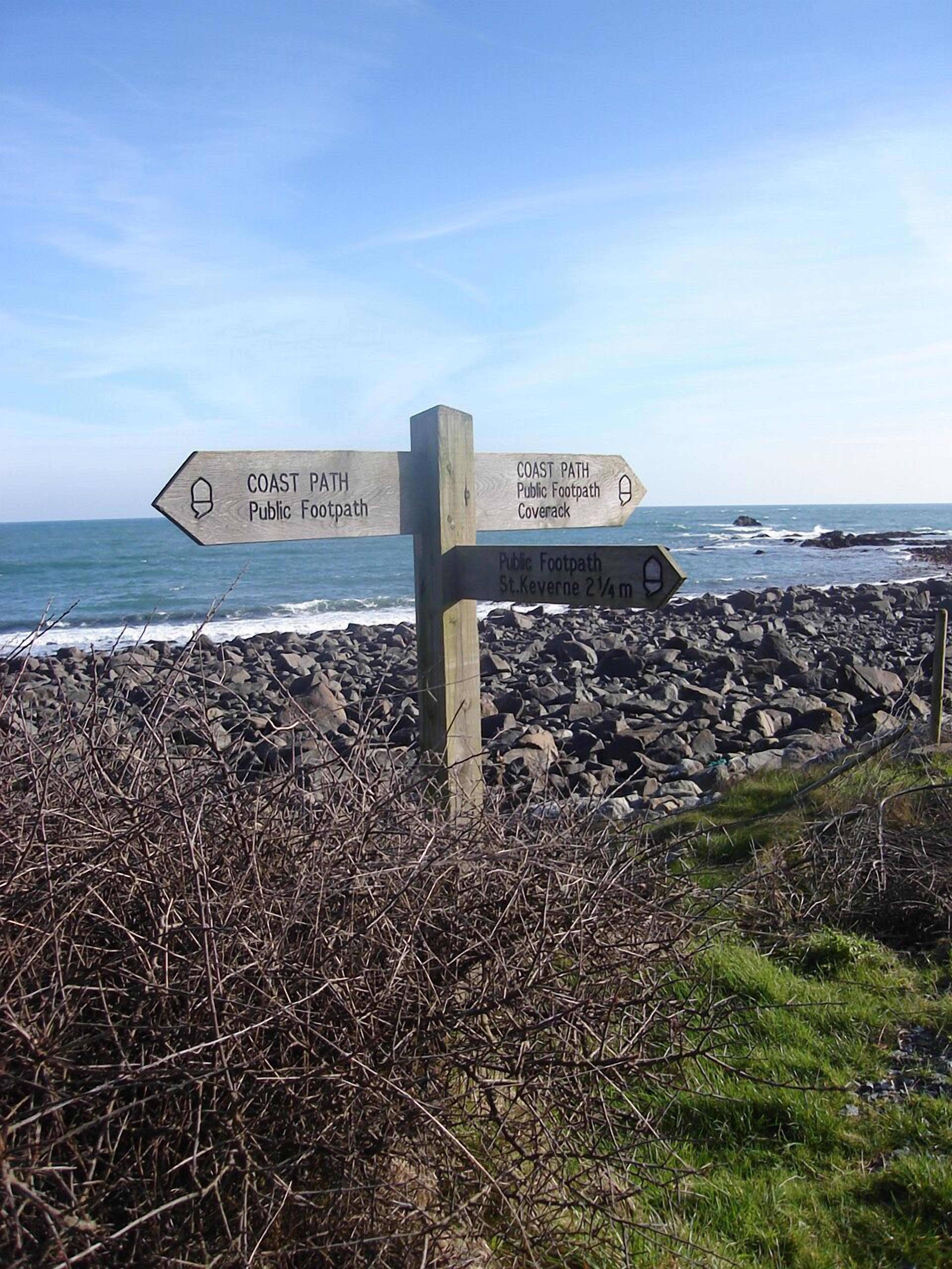 A directional signpost with multiple arrows pointing towards different public footpaths and a coastal path.