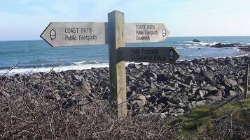 A directional signpost with multiple arrows pointing towards different public footpaths and a coastal path.