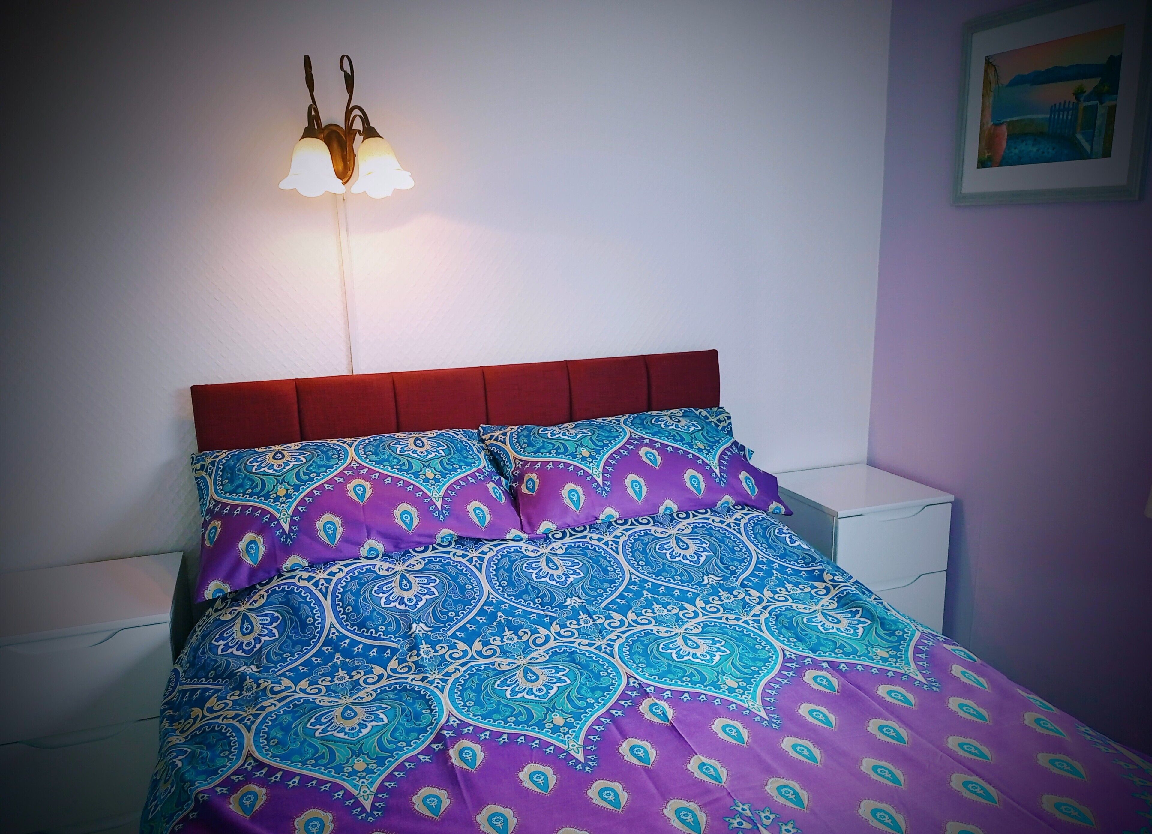 A bed with a patterned bedspread and a red headboard.