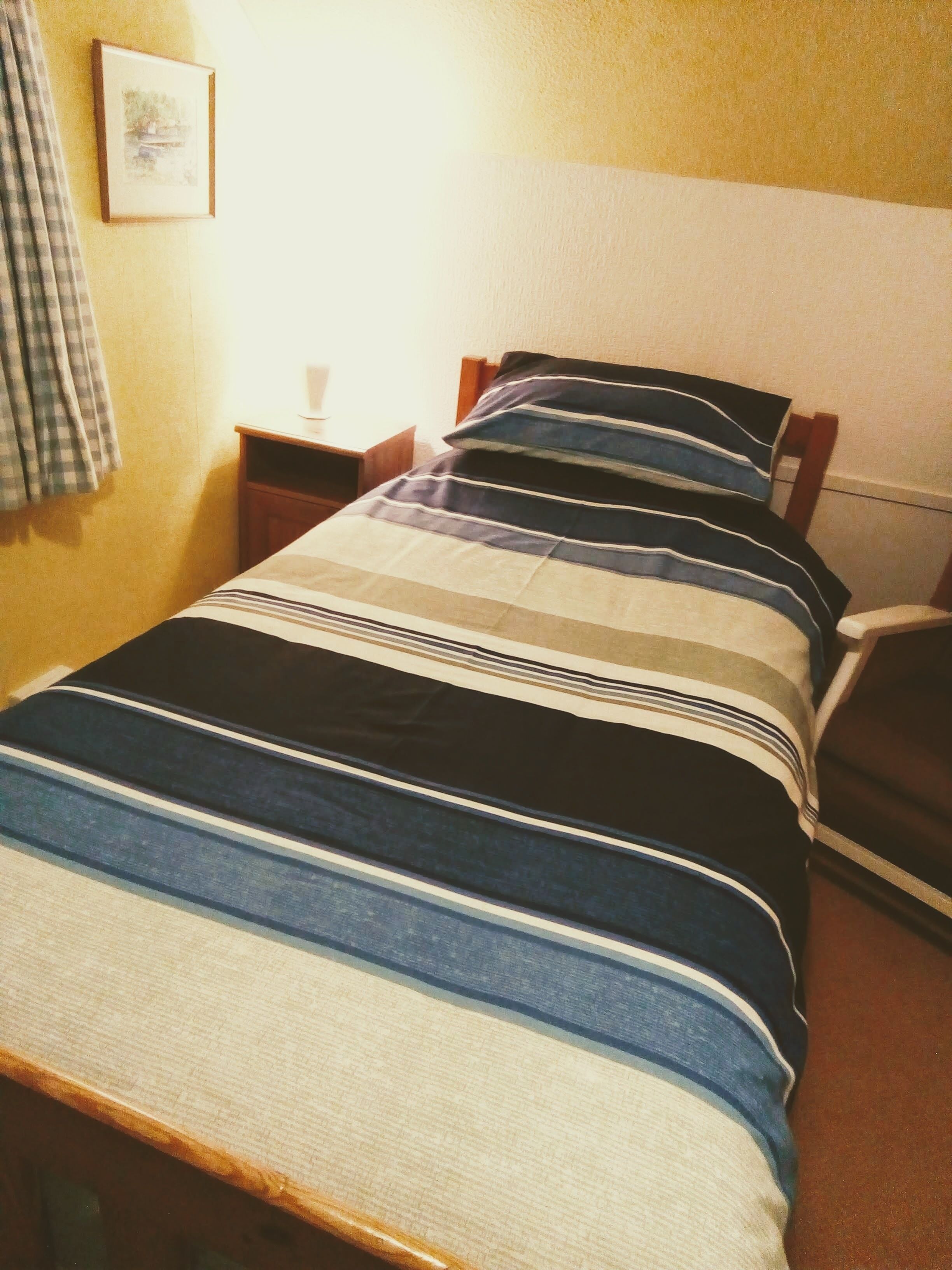 A single bed with a striped bedspread, a bedside table with a lamp, and a chair.
