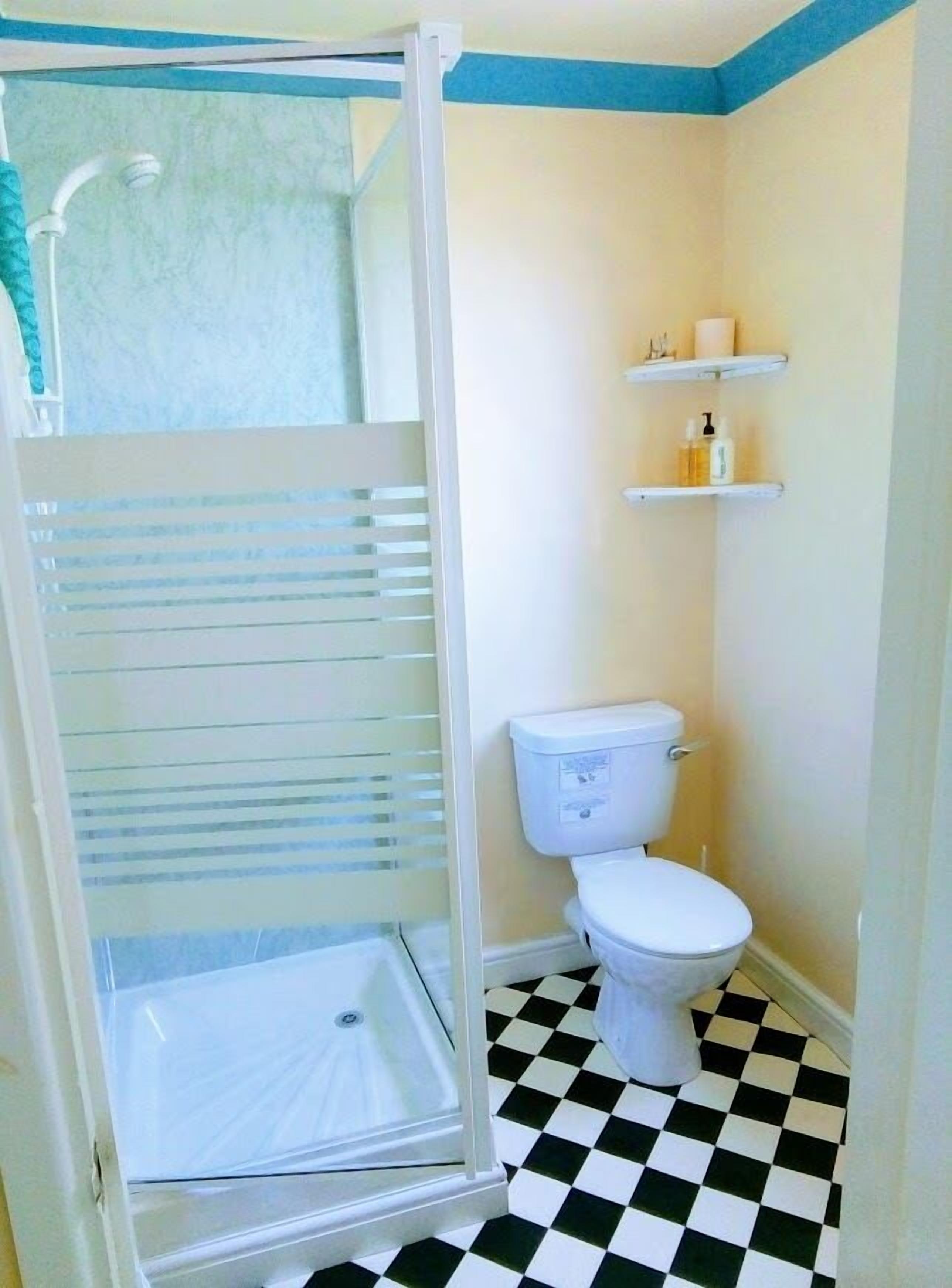 Un baño con inodoro blanco, cabina de ducha y suelo de cuadros.