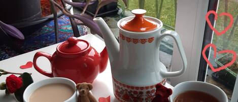 A breakfast setup with a teapot, cups, and chocolates on a table by a window.