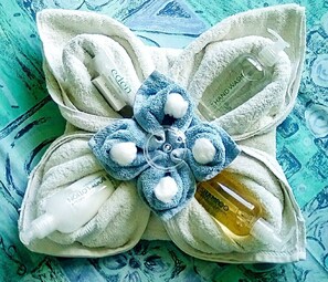 A towel arranged in a flower shape with various toiletries like Eden sewing kit, Nollo R, and shampoo. - Gallen-treath Guest House (Helston)