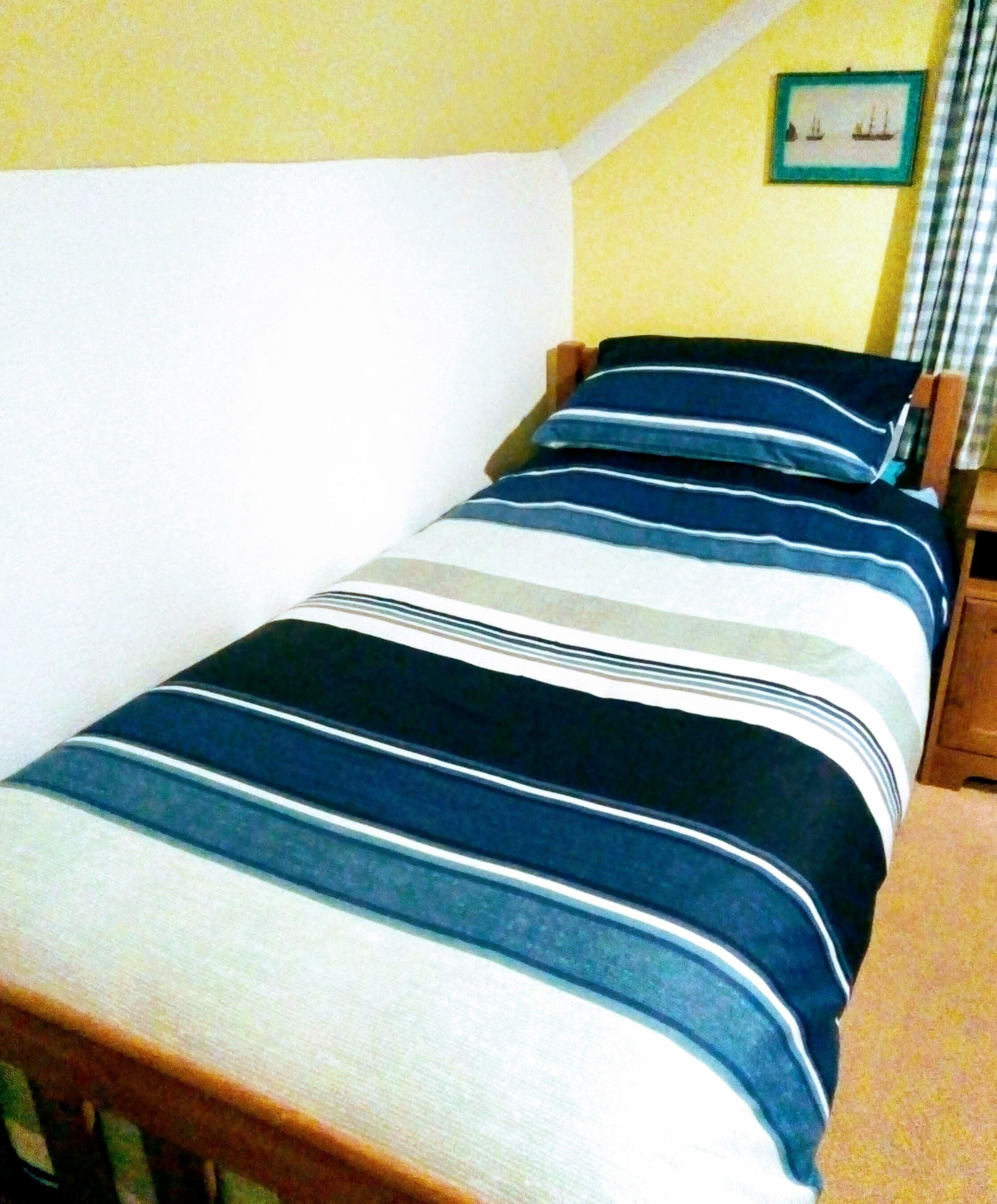 A single bed with a striped bedspread in a room with yellow walls and a framed picture on the wall.