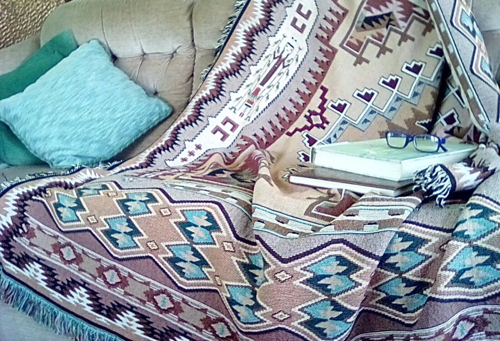 Un sofá con un plaid estampado, una almohada azul y un libro con gafas encima.