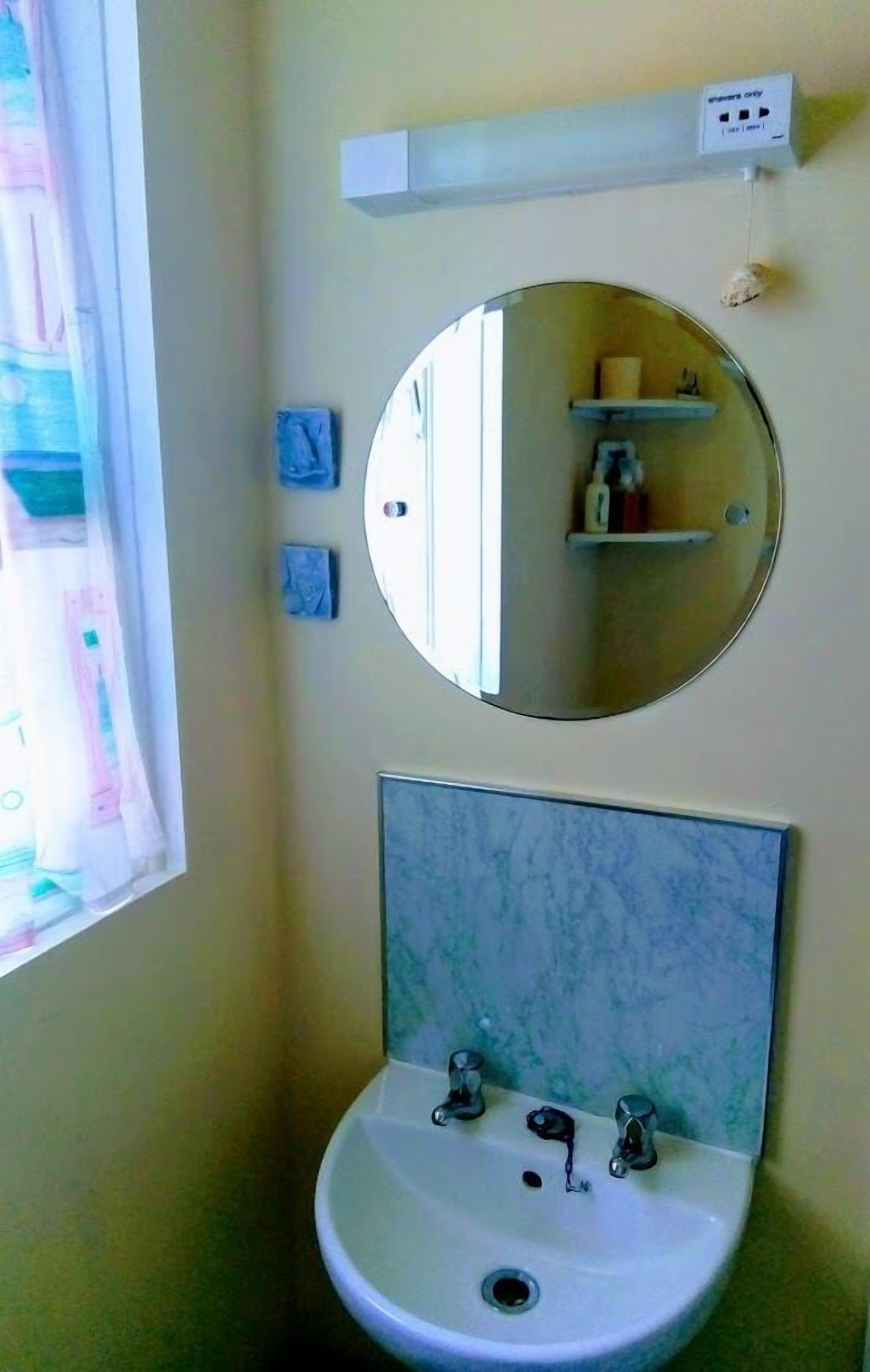 Une salle de bain avec un miroir rond, un lavabo à deux robinets et une étagère au-dessus du miroir.