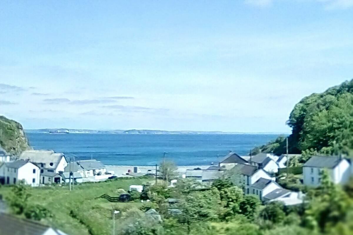 A coastal village with houses along the shore, a clear sky, and the sea in the background.