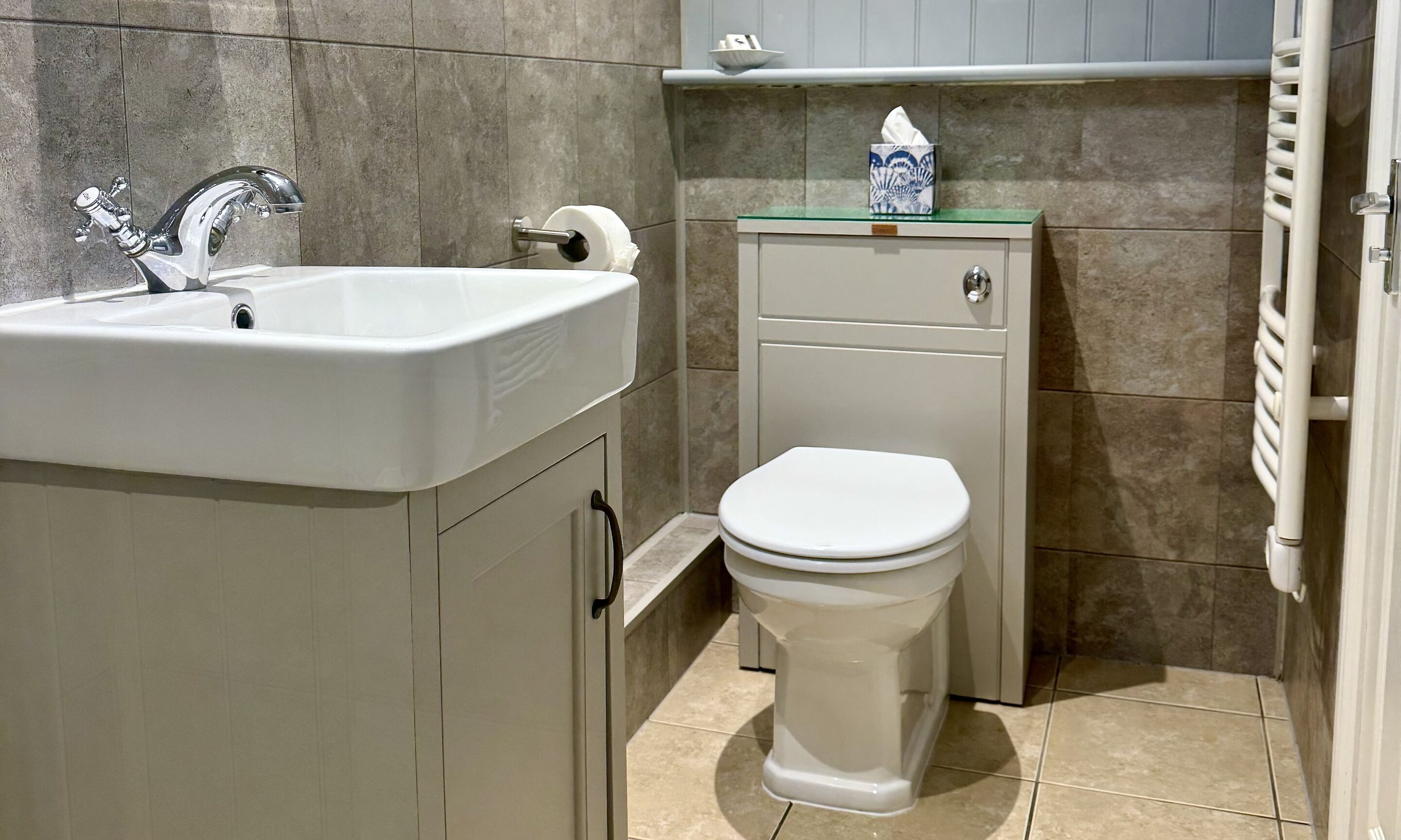 A bathroom with a white sink, a toilet, and a towel dispenser.