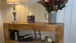A wooden console table with a tissue box, a lamp, a vase with flowers, a coffee maker, and a bottle. - Sibton White Horse Inn (Saxmundham)