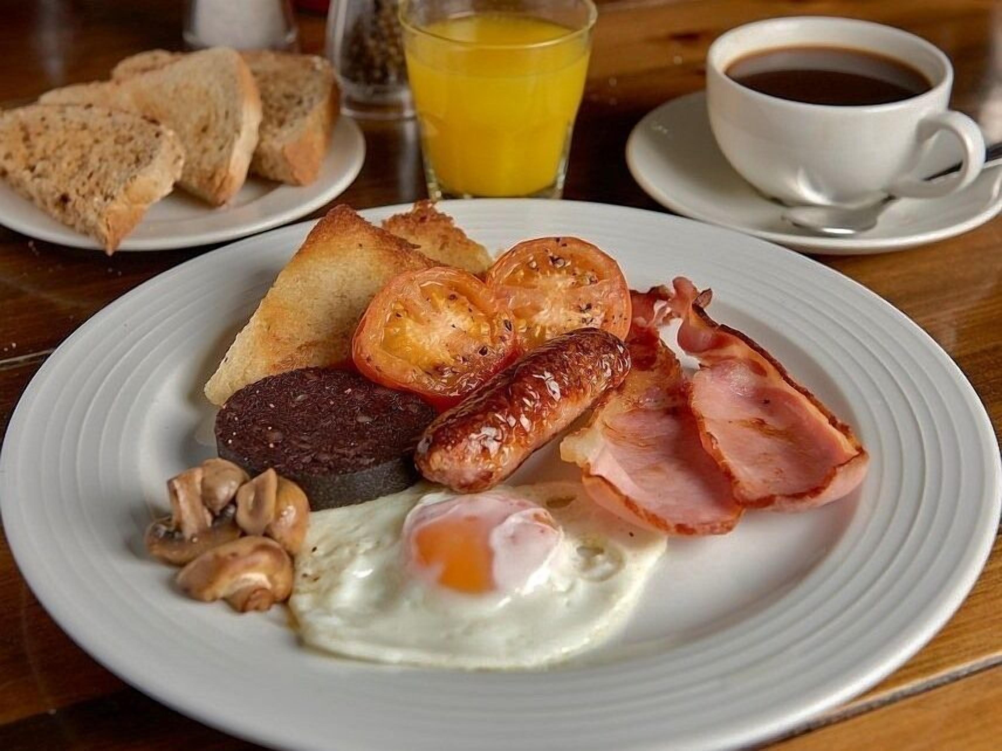 A breakfast plate with eggs, sausages, bacon, mushrooms, and toast.