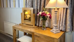 A wooden desk with a mirror, a lamp, and a vase of flowers. - Sibton White Horse Inn (Saxmundham)