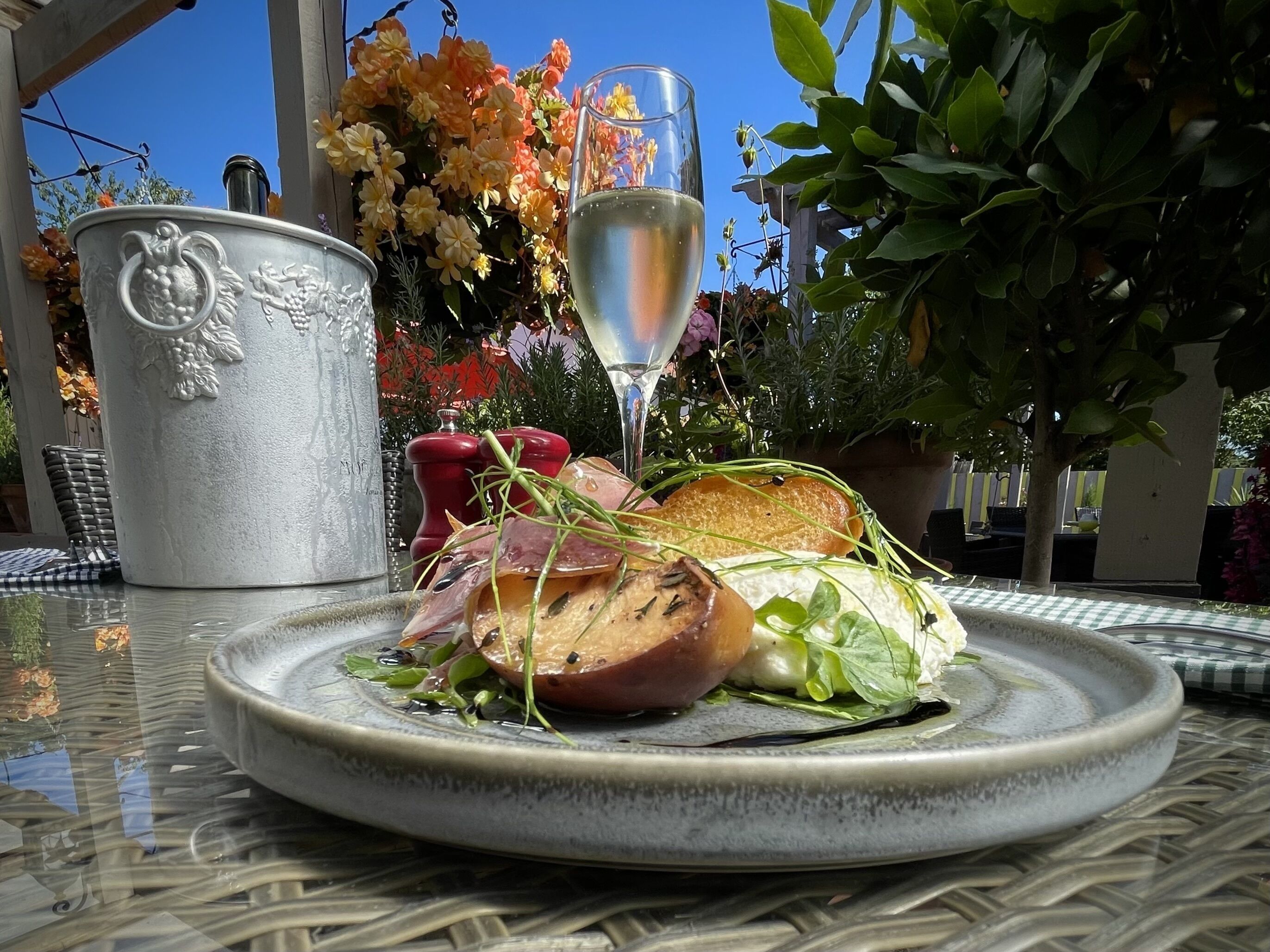 A table with a plate of food, a glass of white wine, and a decorative metal pitcher.