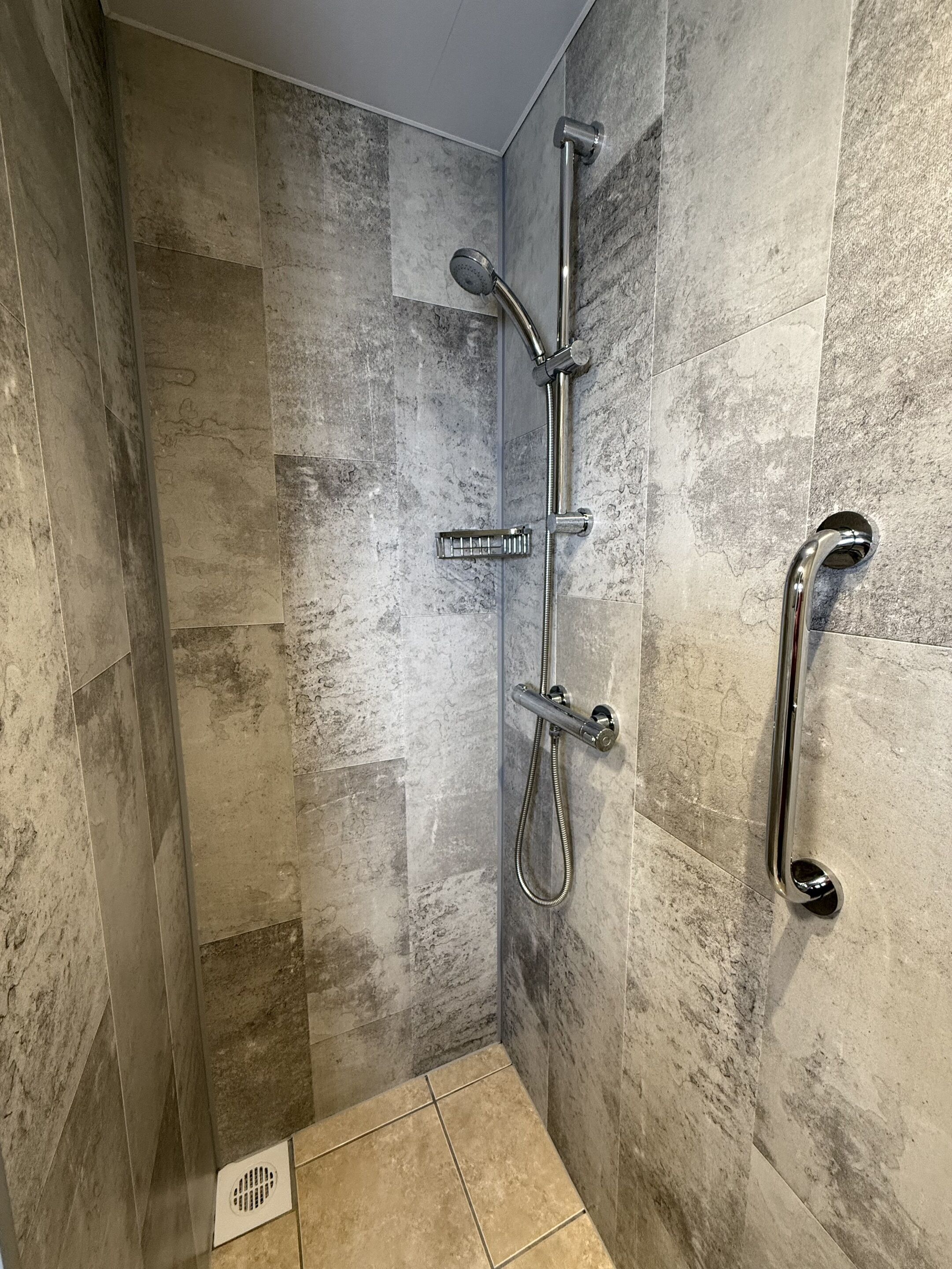 A shower with a handheld showerhead, a wall-mounted faucet, and a handheld showerhead.