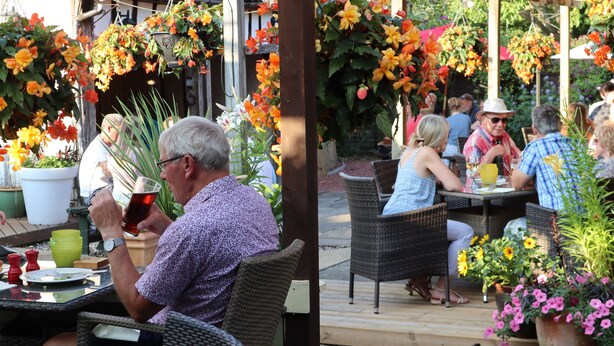 An outdoor seating area with wicker chairs and tables, surrounded by potted plants and hanging flower baskets. - Sibton White Horse Inn (Saxmundham)