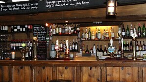 A bar with wooden walls, multiple liquor bottles, and a variety of taps. - Sibton White Horse Inn (Saxmundham)