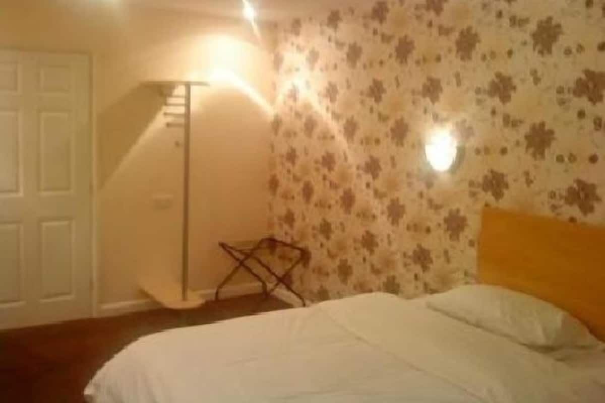 Quarto com cama, porta branca, abajur e parede com padrão floral.