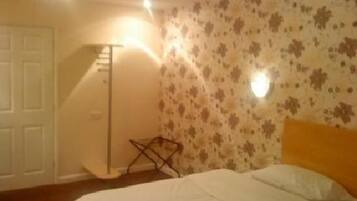 Une chambre à coucher avec un lit, une porte blanche, une lampe sur pied et un mur orné d’un motif floral.