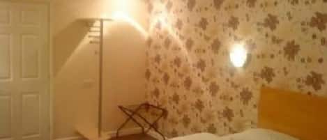 A bedroom with a bed, a white door, a floor lamp, and a wall with a floral pattern.