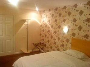 A bedroom with a bed, a white door, a floor lamp, and a wall with a floral pattern. - Ashiana Hotel (Newark)