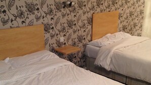 Two single beds with wooden headboards, a small bedside table, and floral wallpaper. - Ashiana Hotel (Newark)