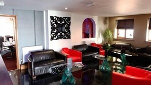 A modern living room with black and red leather sofas, a glass coffee table, and a decorative mirror. - Ashiana Hotel (Newark)