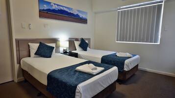 Quarto de hotel com duas camas, um quadro de montanhas, ar condicionado e uma janela com persianas.