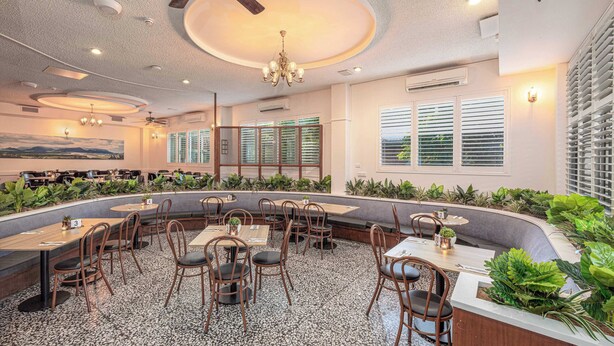 Un restaurante con una zona de estar curva, varias mesas y sillas. Hay ventiladores de techo e iluminación empotrada.