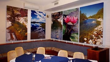 Uma sala de conferências com uma mesa comprida, quatro grandes pinturas de paisagens e cadeiras de vime.