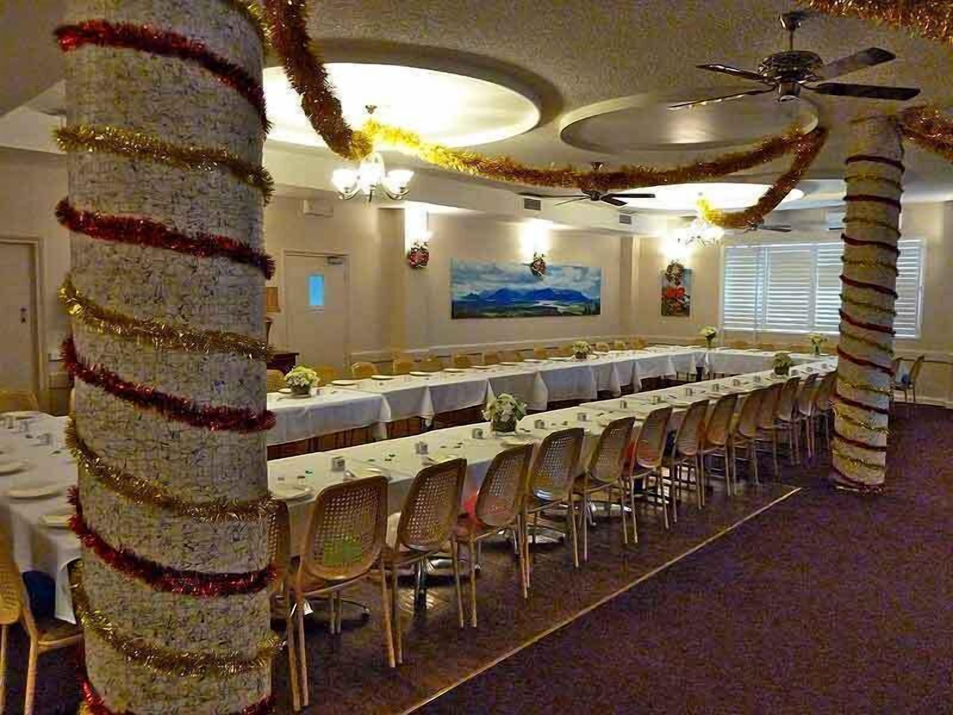 Une salle de banquet avec de longues tables, des chaises et un ventilateur de plafond.